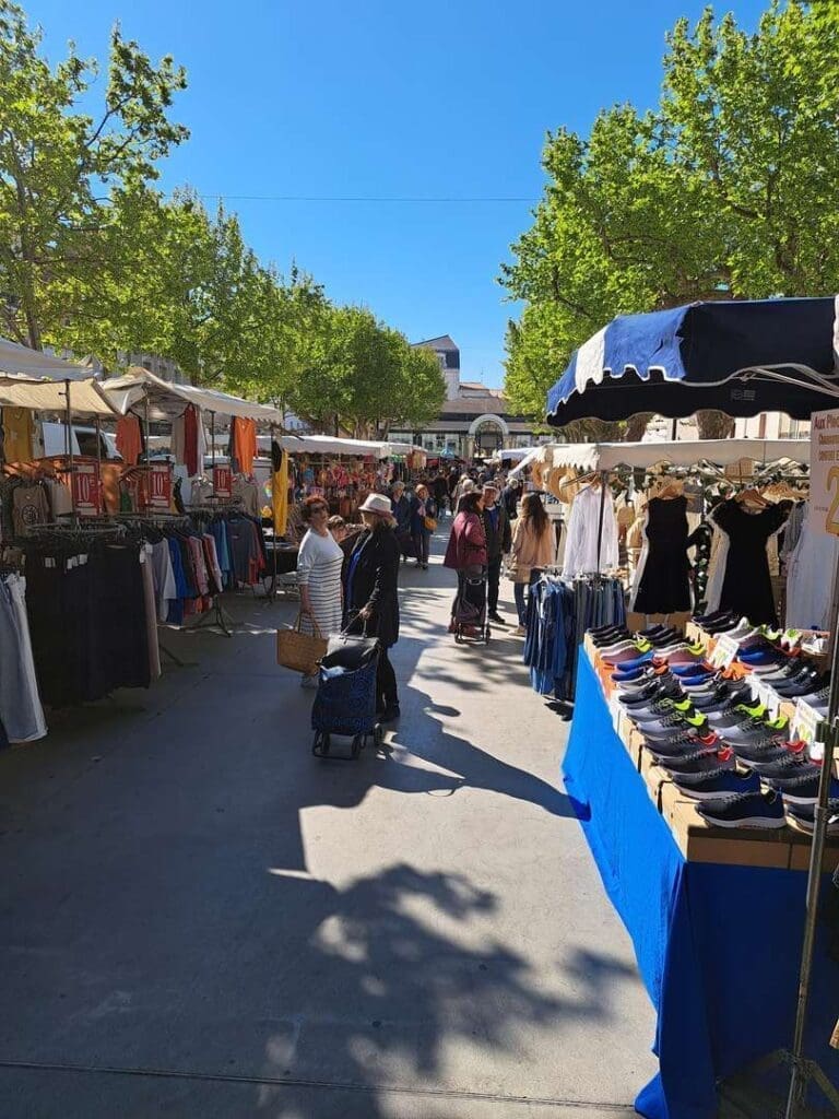 Allée d'un marché en plein air à Mèze, étals de vêtements sous les arbres