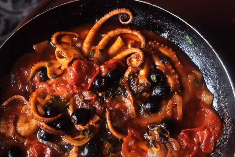 Poulpe de roche mijoté aux tomates cerises, olives noires et persil dans une poêle en fonte