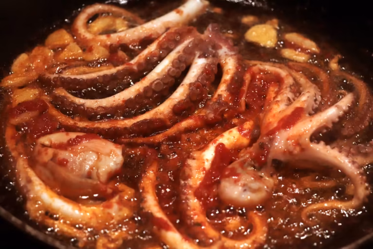 Poulpes de roche entiers qui cuisent dans la poêle avec l'ail avant les tomates