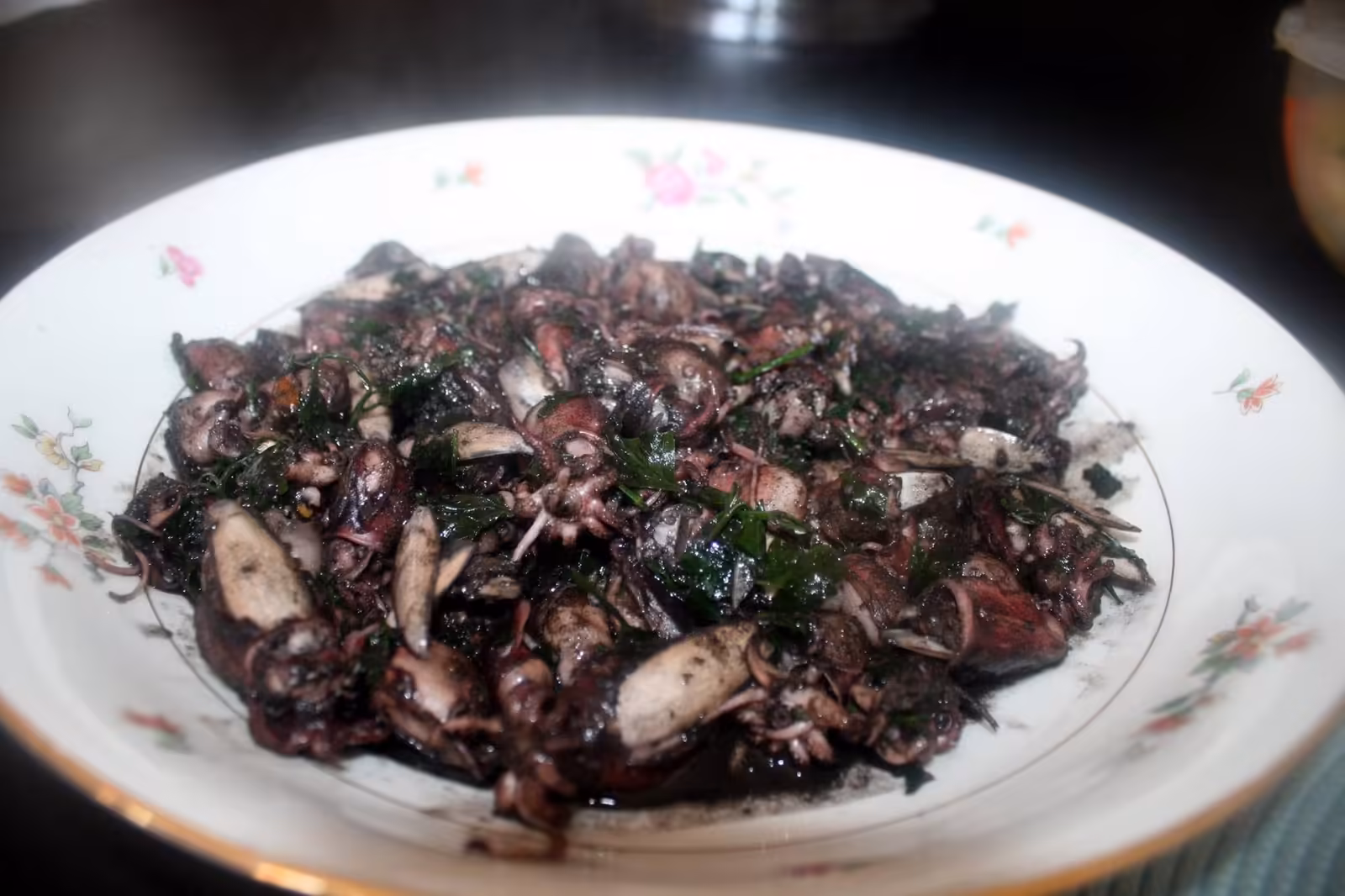 Supions à l'encre servis dans une assiette creuse fleurie, persil haché par dessus